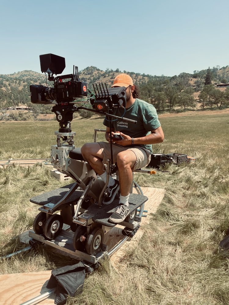 Kaalob Justin Moran running a cinema camera on a dolly track during an outdoor film shoot